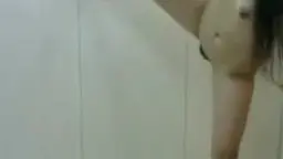 Nackte Asiatin mit langen Haaren kniet auf gestreiftem Bett und hält großen weißen Dildo in beiden Händen.