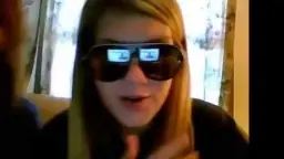 Zwei junge Blondinen schauen frech in die Kamera, eine mit reflektierender Sonnenbrille, enge schwarze Shirts, helle Wohnung im Hintergrund