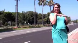 Schwangere Frau mit langen dunklen Haaren und türkisfarbenem Kleid steht vor Palmen in der Sonne
