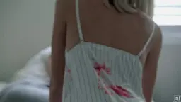 Blondes Mädchen von hinten in durchsichtigem weißem Negligé mit roten Blüten, steht verführerisch im Schlafzimmer.