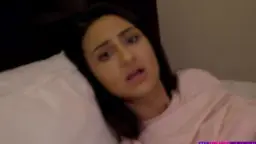 Reife Frau mit dunklen Haaren liegt mit offenem Mund und lustvollem Blick auf weißen Kissen