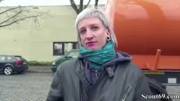 Blonde Frau mit grünem Schal und Lederjacke läuft auf Kopfsteinpflaster an einem Lkw vorbei